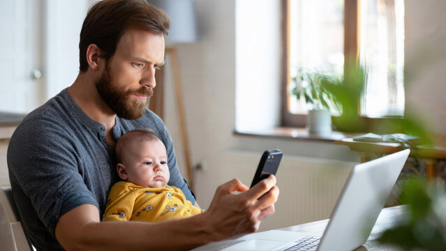 Remote working dad, multitasking parent with baby, digital nomad family, home office with infant, laptop lifestyle parenting, work from home dad, mobile work life, family workspace indoors