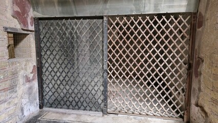 Herculaneum, Italy - 9 January 2025. Latticed wooden gates seal off a chamber in an ancient Roman house, preserving its interior.