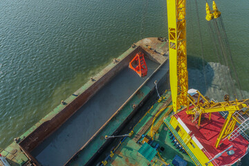 Drone photo showing a crane barge lifting dredged material into a barge during marine maintenance...