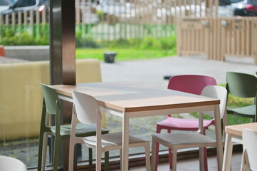 Clean Nordic-style dining area featuring white plastic chairs overlooking lush green outdoor space. Minimalist restaurant interior design with natural daylight and garden view.