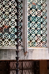 Traditional rain chain featuring connected cups for guiding rainwater from eaves, positioned against decorative window with intricate geometric patterns creating architectural detail composition.