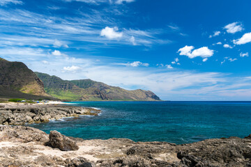 Scenic view of Makua Beach on the west coast of Oahu, Hawaii, with lush green mountains and dramatic clouds above 