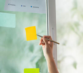 Close-up of hand placing sticky note on window for task management