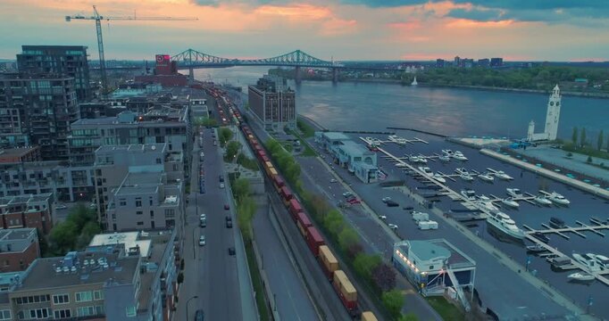 Aerial view of Montreal, Canada, featuring the Jacques Cartier Bridge, a train, and a marina at sunset. The photo captures the city's infrastructure and waterfront.