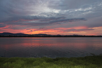 Fototapeta premium A breathtaking sunset over a calm river with vibrant orange and purple hues painting the sky. A small boat glides across the water, leaving gentle ripples under the silhouette of distant mountains.