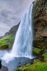 Seljalandsfoss waterfall in Iceland with lush green surroundings and a cloudy sky
