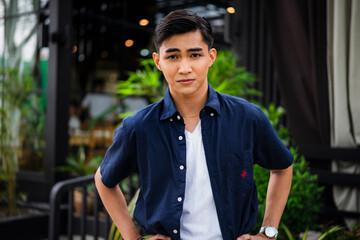 A young cocky Asian man with hands on his waist and a slight frown, showing smug attitude while...