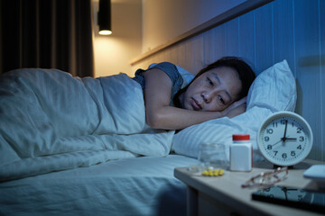 Female Asian middle-aged person has a sleep disorder, is stressed, and worries awake at night from drug side effects, insomnia illness in bedroom, mature and menopausal woman's healthcare problem.