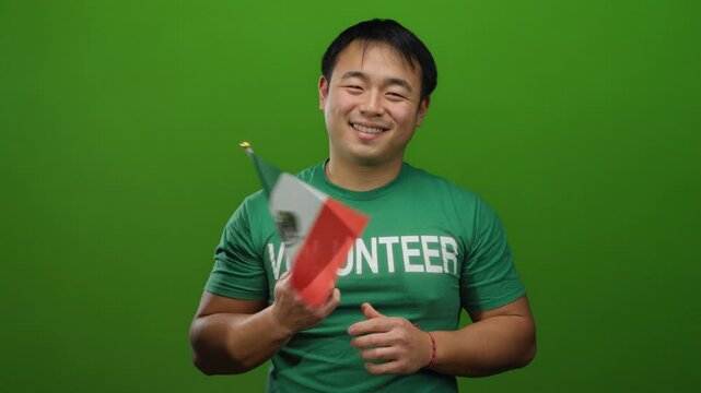 Man smiling holding mexico flag wearing volunteer shirt against green background isolated cheerful young.