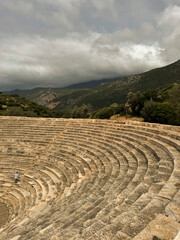 Ancient theater nestled in mountainous region with dramatic cloudy sky overhead