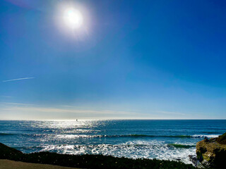 Sunny Ocean View with Sailboat and Rocky Shore
