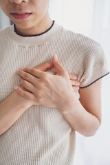 A woman places her hand on her chest, experiencing chest pain from a heart attack. Healthcare and...