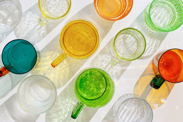 Colorful glowing glass cups on white background, casting artistic light reflections and shadows in...
