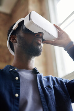 Low angle view of African young man in VR goggles playing video game or watching something online