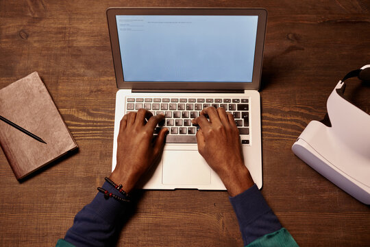 High angle view of African businessman sitting at wooden table and working on laptop, he typing document online