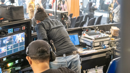 Backstage production team operating broadcast monitors and audio mixer during live event to manage...