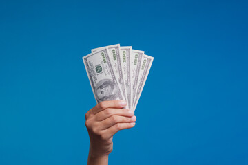 Hand holding five 100 dollar bills on blue background symbolizing financial success and wealth.