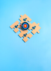 Teamwork concept with jigsaw puzzle pieces with human icons and target symbol on blue background, representing stakeholder alignment, cooperation, business goal, synergy, collaboration, team building.