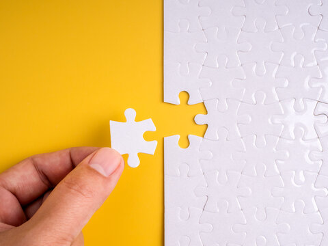 Close-up hand placing last puzzle piece into missing spot on yellow background, symbolizing solution, problem solving, completion, final step, teamwork, integration, and strategic fit in business. - Powered by Adobe