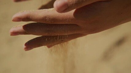 Two hands pour warm beach sand, creating a gentle cascade. Sunlight shines on the golden grains, capturing the feeling of relaxation and enjoyment by the shore.