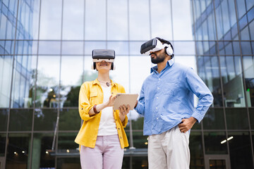 Two people wearing VR headsets are standing in front of a modern building, likely exploring virtual reality with a tablet.