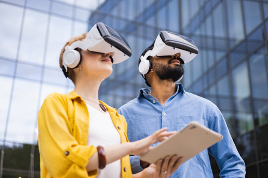 A diverse pair experiences virtual reality outdoors, exploring modern technology near a glass-walled building. - Powered by Adobe
