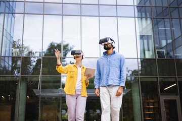 Two people wearing VR headsets exploring virtual reality near a modern building.