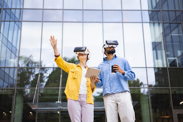 Two people wearing VR headsets explore virtual reality together in front of a modern glass building.