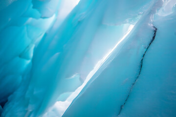 Abstract close up of vibrant turquoise blue glacial ice formations with light shining through deep crevasses and textures creating a cool natural background