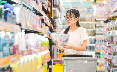 Young adult asian woman customer choosing laundry liquid detergent from household shelf shopping at...