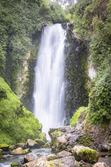 Majestic Peguche waterfall in Otavalo, Ecuador. Water cascades powerfully among moss-covered rocks and vibrant greenery, reflecting the purity of Andean nature.