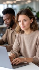 Young woman of European descent and man of African ethnicity working together on laptops in a modern office, focused on work 