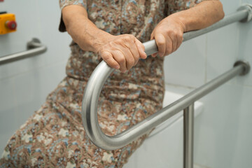 Asian elderly woman patient use toilet support rail in bathroom.