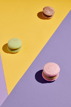 Vertical image of sweet colorful macaroons on geometrical backgrounf purple and yellow colors
