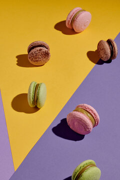 Vertical image of sweet french macaroons isolated on geometrical background with yellow and purple colors