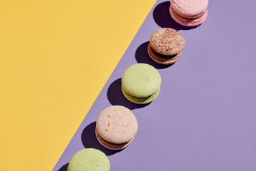 Horizontal image of colorful fresh macaroons lying on a row against the purple and yellow background
