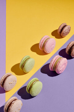 Vertical image of colorful sweet macaroons lying in two rows against the purple and yellow background