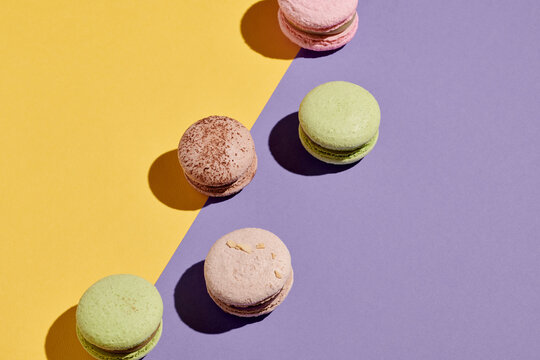 Horizontal image of french macaroons lying in a zigzag line over purple and yellow background