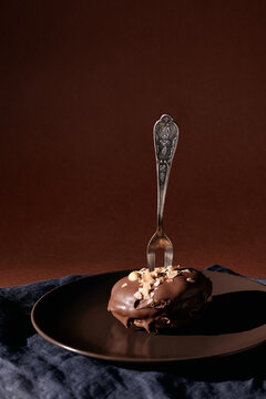 Vertical image of chocololate cake with nuts and dessert fork on it served on the plate isolated on brown background