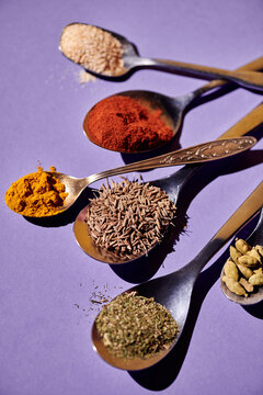 Vertical image of large numbers of spoons with different spices for preparing food isolated on purple background