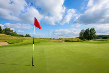 Obraz premium Red flag on a golf course with green grass and blue sky