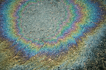 Gasoline or oil spill creates rainbow sheen on asphalt road surface