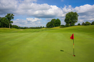 Golf green with flag and manicured grass under a cloudy sky