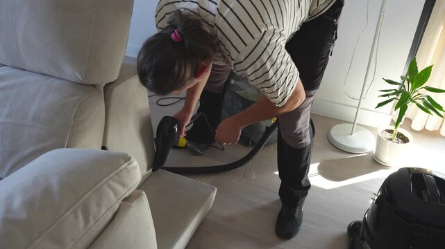 Top down shot of a male cleaner worker drying the fabric of the sofa with a hair dryer after using a special machine with ionized water
