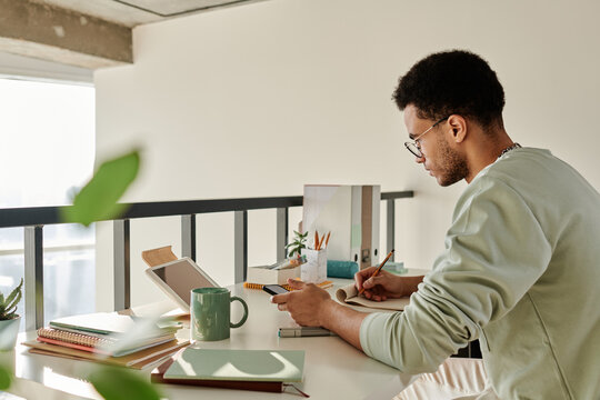 Horizontal image of college student sitting at desk and studying at home using digital tablet in his study