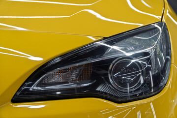 BI-LED headlights of a modern and expensive yellow car. Front BI-LED headlight on a yellow sport car. Gloss yellow premium car BI-LED headlights close-up. Modern sport car headlight. 