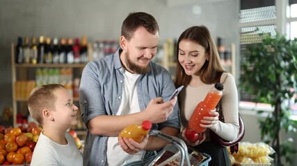 Young bearded man with wife and tween son buying organic bottled juices in grocery shop, scanning QR codes on bottles using smartphone to add items to digital cart and process online payment - Powered by Adobe