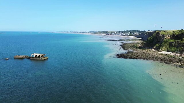 From above, the vestiges of the Arromanches artificial harbour appear in geometric shapes, stretching into the sea