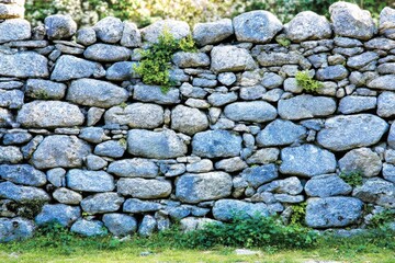 Ancient stone wall with rounded stones and greenery
