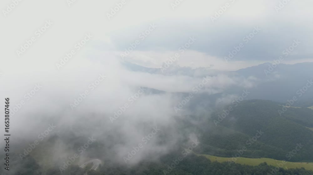 Poster a view of a mountain range partially covered by clouds the sky is overcast and the landscape is gree